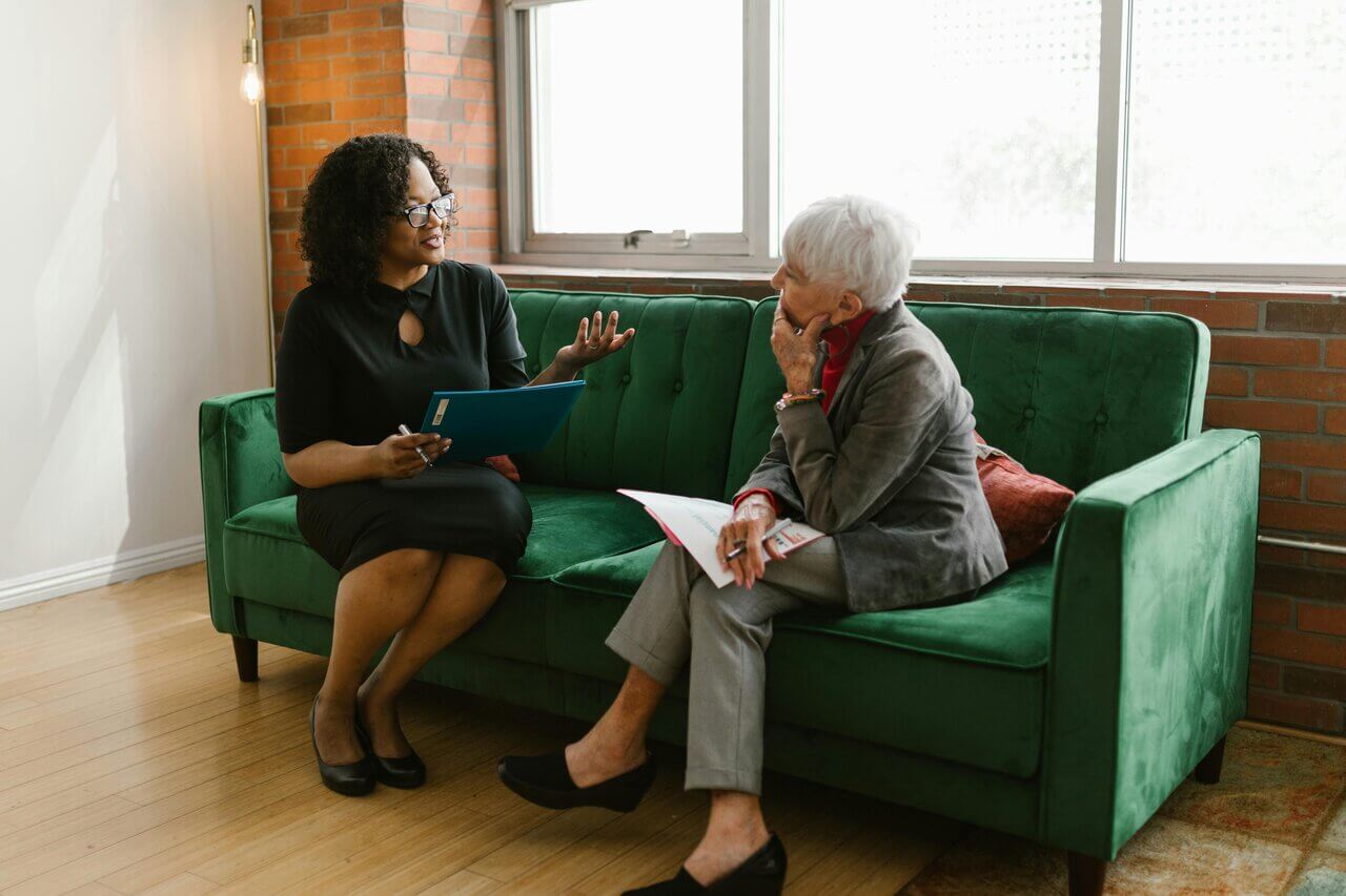 Two female middle aged professionals sitting on sofa in workplace conversating