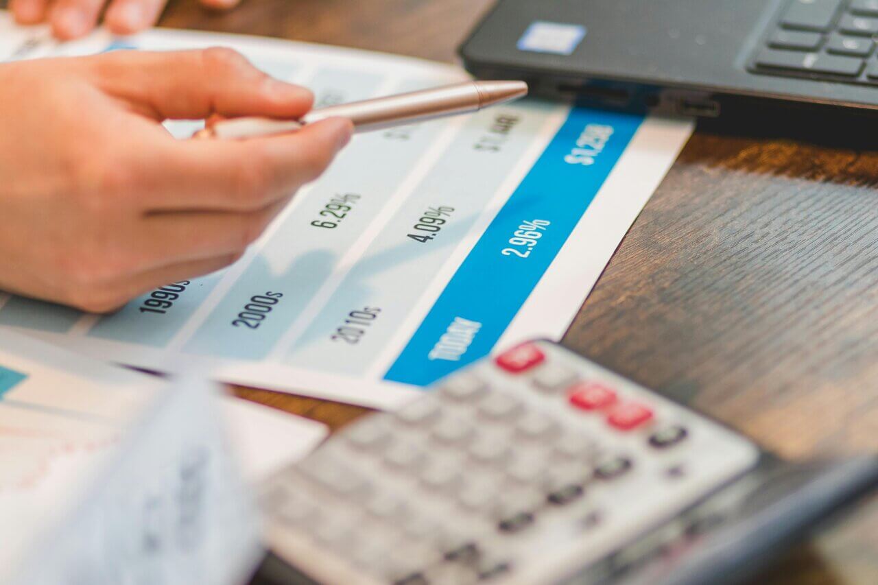 Close up of hand with pen across desk, with documents and calculator