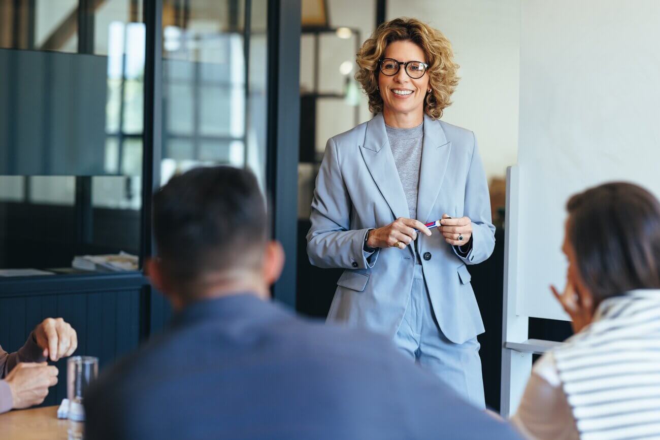 Middle aged woman standing in front of colleagues smiling