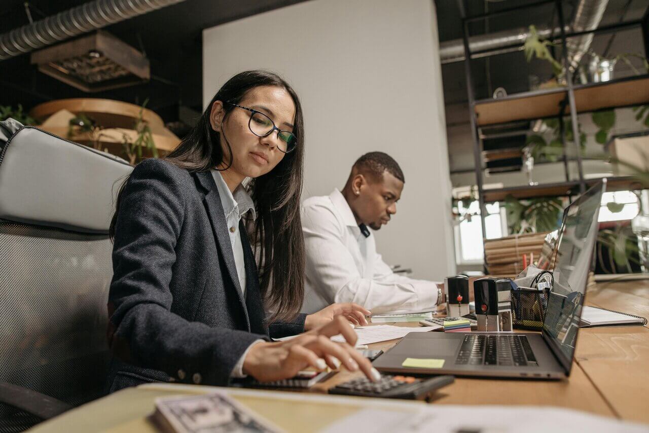 Two professionals at desk on laptops with calculator