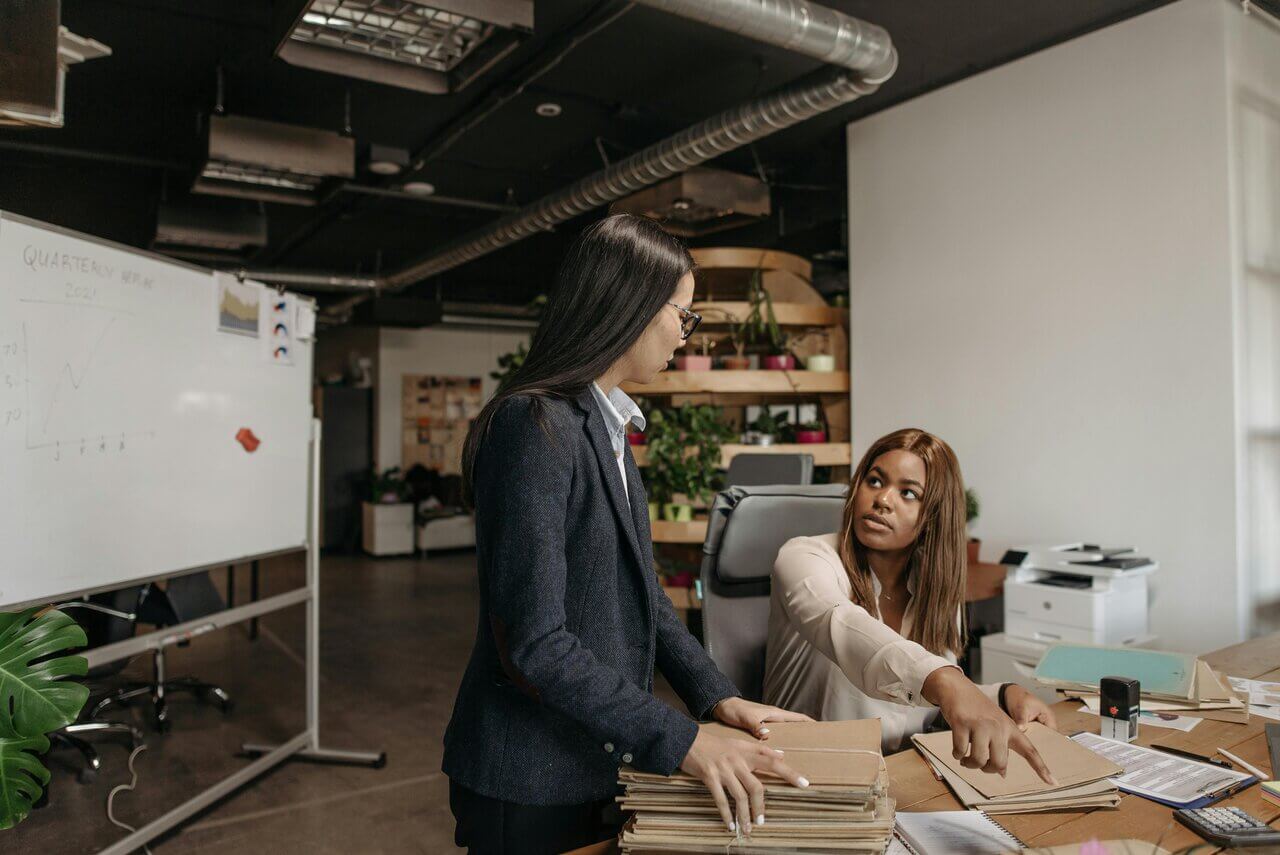 Two female professionals in office space discussing files